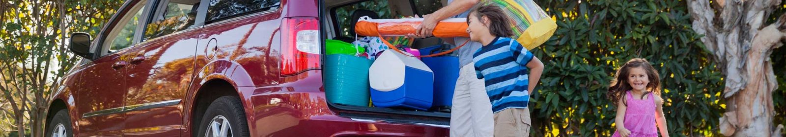 Family vehicle backed with items for a road trip. Kids smiling outside of car.